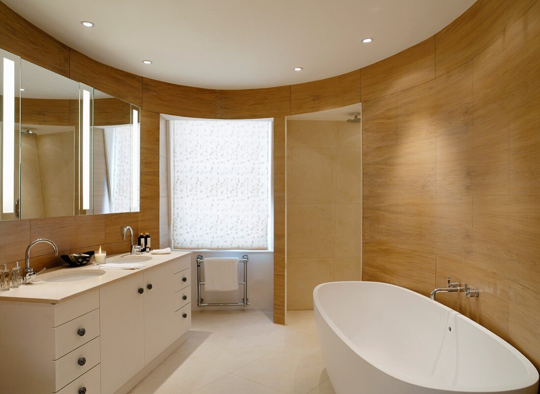 Free-standing bathtub in oval, modern bathroom with wood-panelled walls
