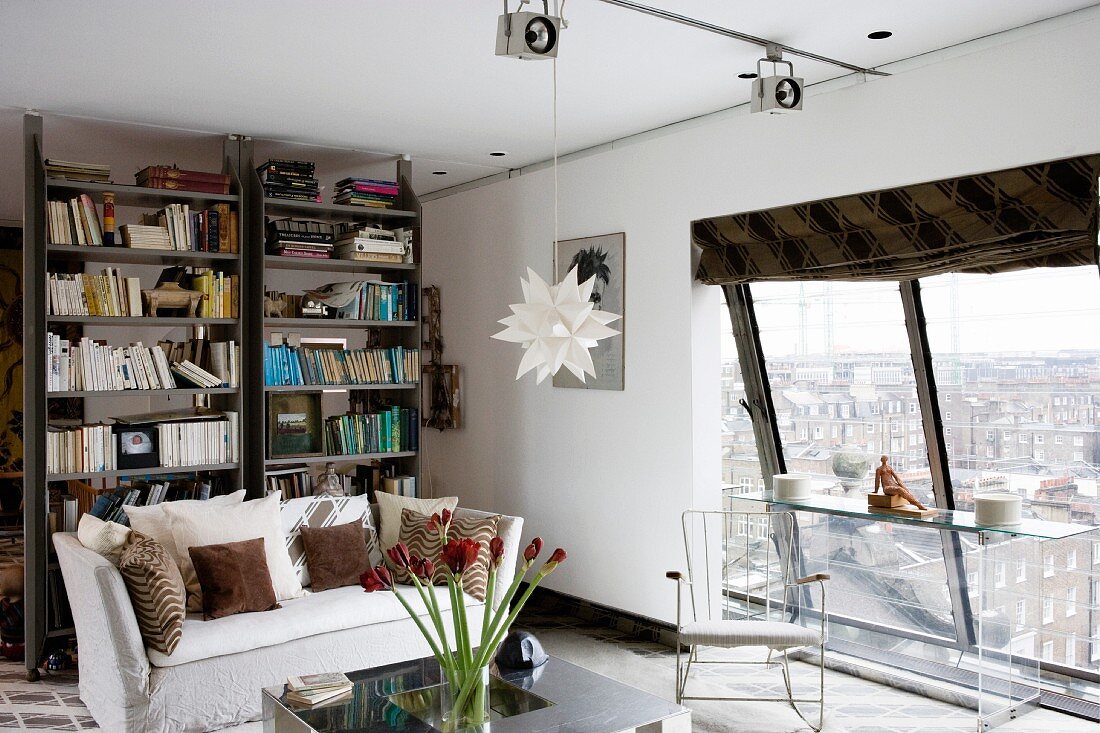 Modernes, junges Wohnzimmer mit Blick durch schräges Panoramafenster auf städtische Kulisse