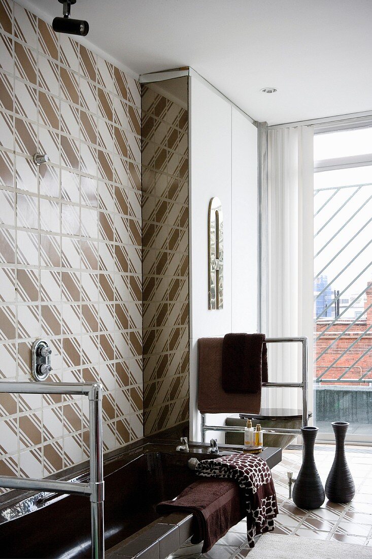 Dark brown bathtub and stainless steel towel rail against 70s, retro-style brown and white tiled wall