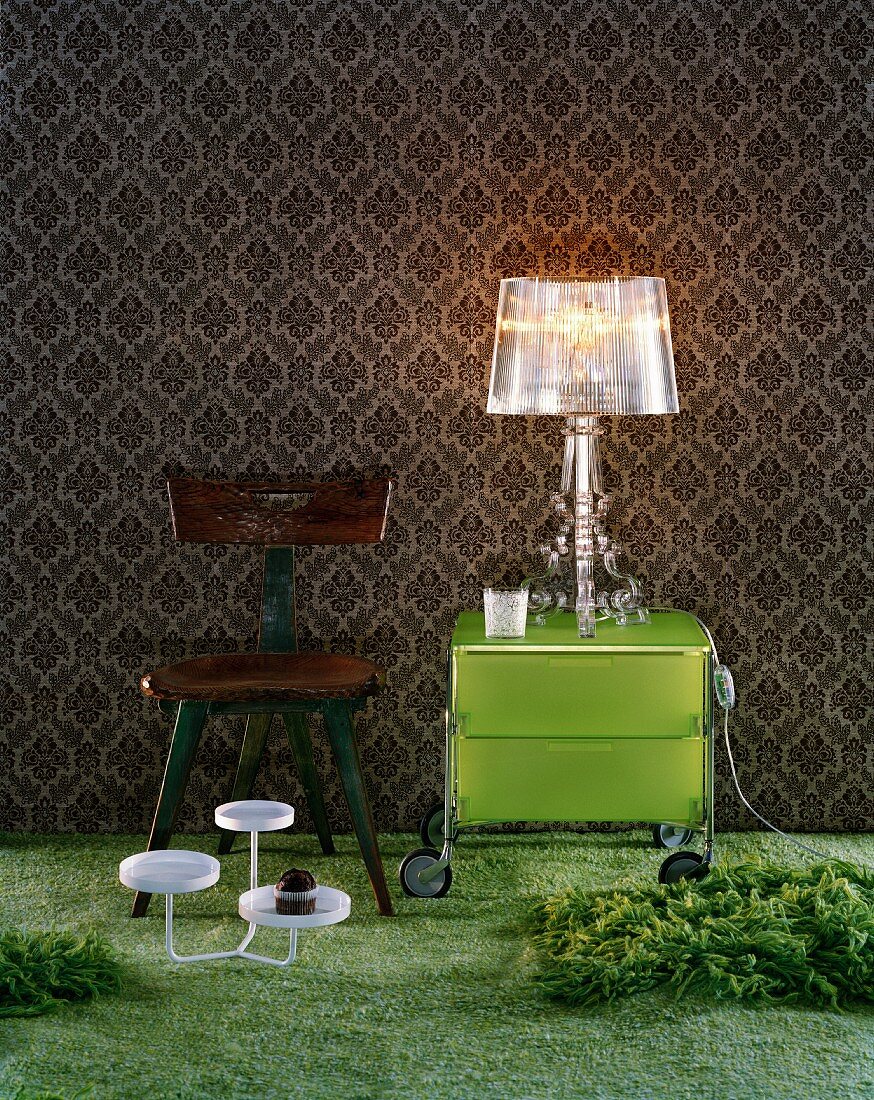 Wallpaper with traditional pattern as backdrop for acrylic glass lamp on modern, grass green, Italian designer cabinet with castors