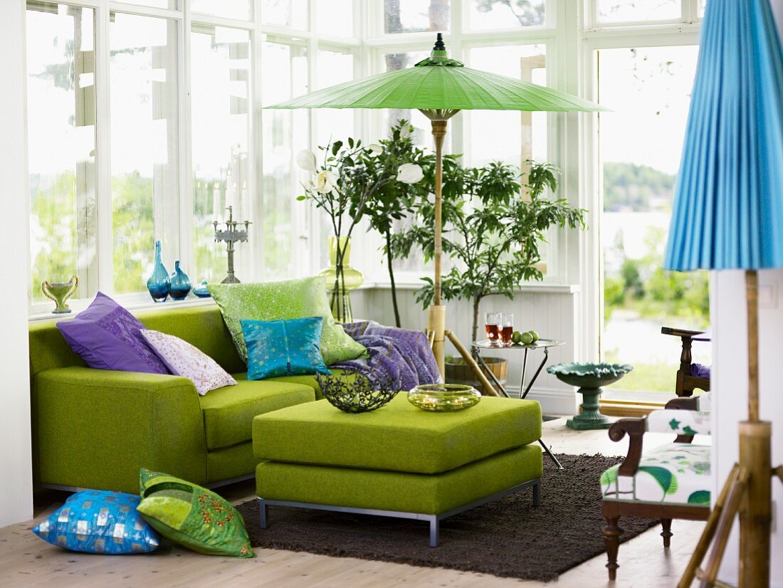 Conservatory atmosphere with colourful cushions on grass green sofa and Oriental paper parasol