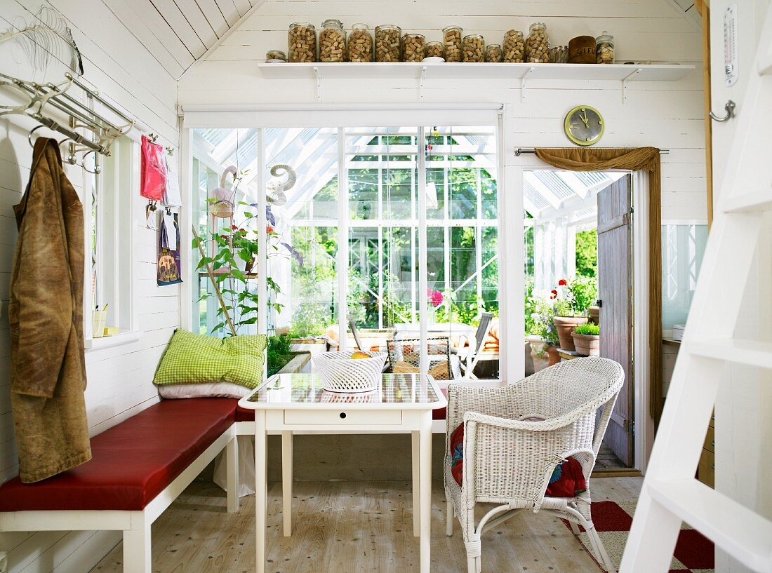 Dining area with bench in rustic, white cabin interior with view of adjacent conservatory