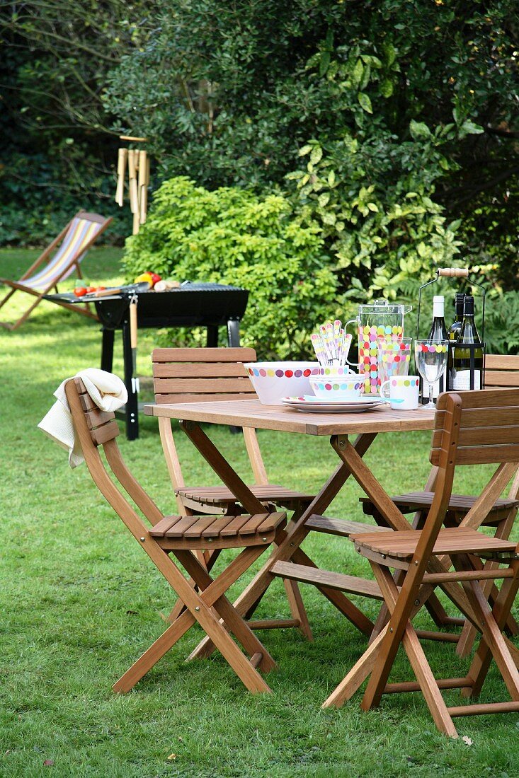 Gedeckter Tisch im Garten mit Stühlen & Grill im Hintergrund