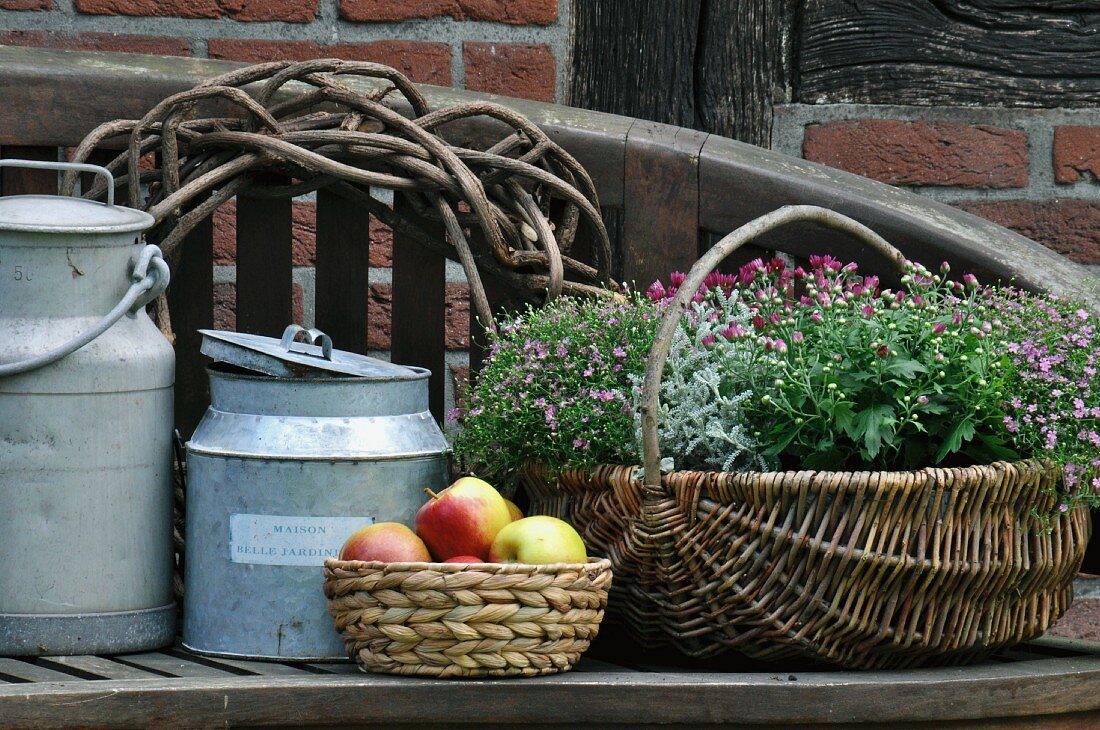 Old milk cans, fruit basket & basket of flowers on wooden bench