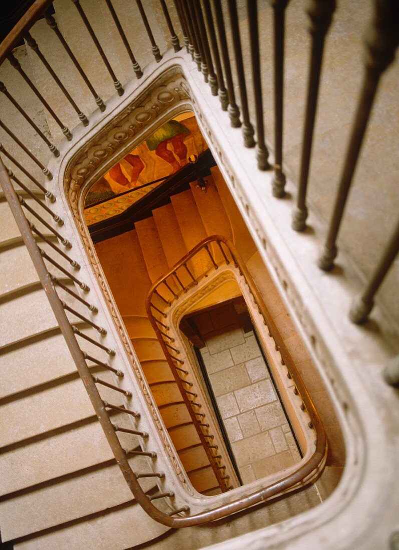 Blick durch rechteckiges Treppenauge mit filigranem Metallgeländer in historischem Gebäude