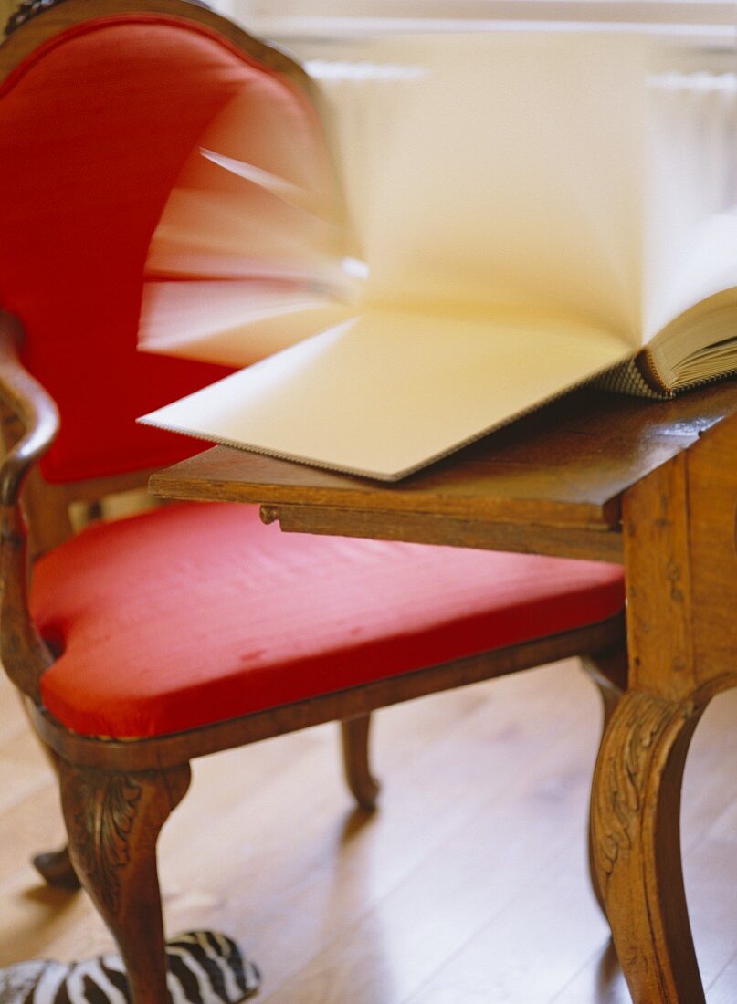 Antique ensemble of desk and chair with red upholstery and book with riffling pages