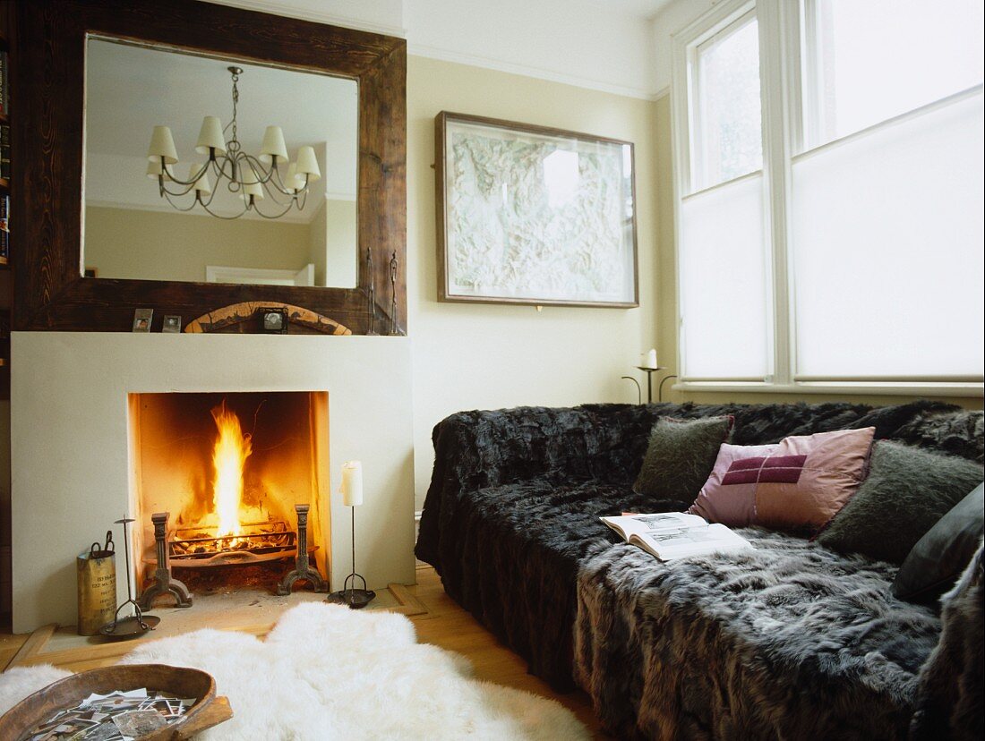 Comfortable oversize sofa with modern faux-fur blankets next to burning fire in fireplace of traditional living room