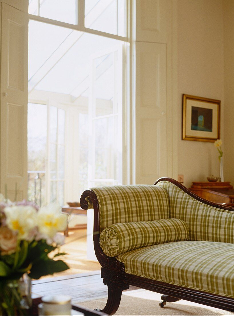 Antique recamier with carved wooden frame and checked upholstery in traditional, sunny apartment in period property