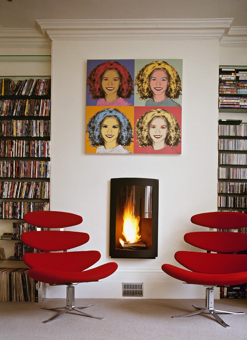 Library with red, modern swivel chairs and pop art pictures above burning open fire