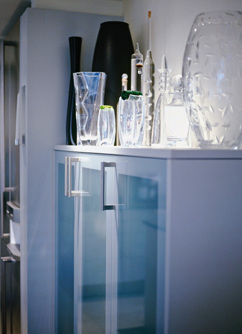 Modern kitchen cupboard with glass doors, spotlights on collection of glass vases