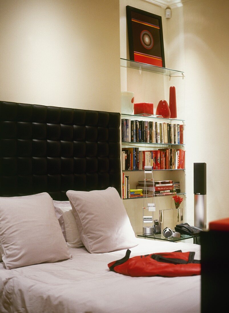Stylish black and white room with red accessories - glass shelves in niche and double bed with cushioned headboard