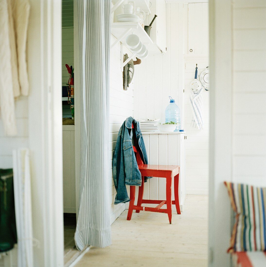 Neben Durchgang mit weißem Vorhang rot lackierter Küchenstuhl und umgehängte Jacke