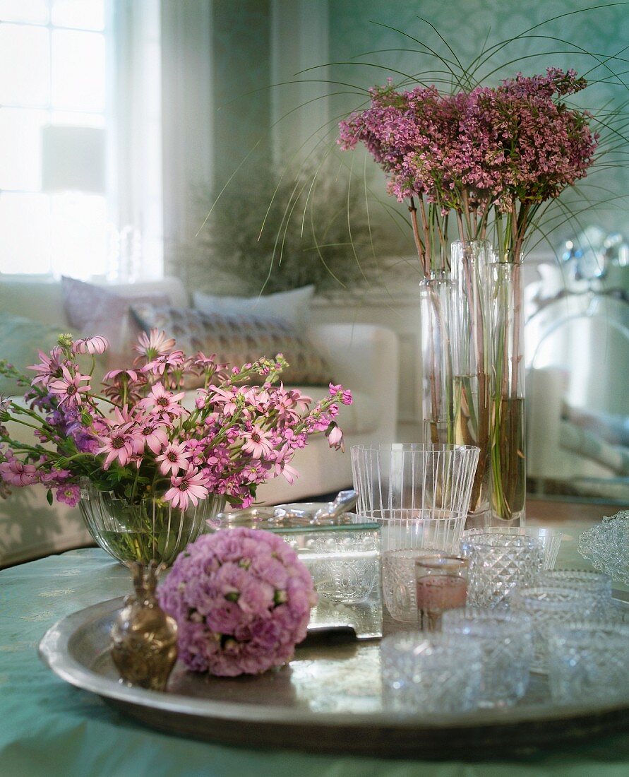 Violette Blumensträusse und Windlichter aus Kristallglas auf Silbertablett