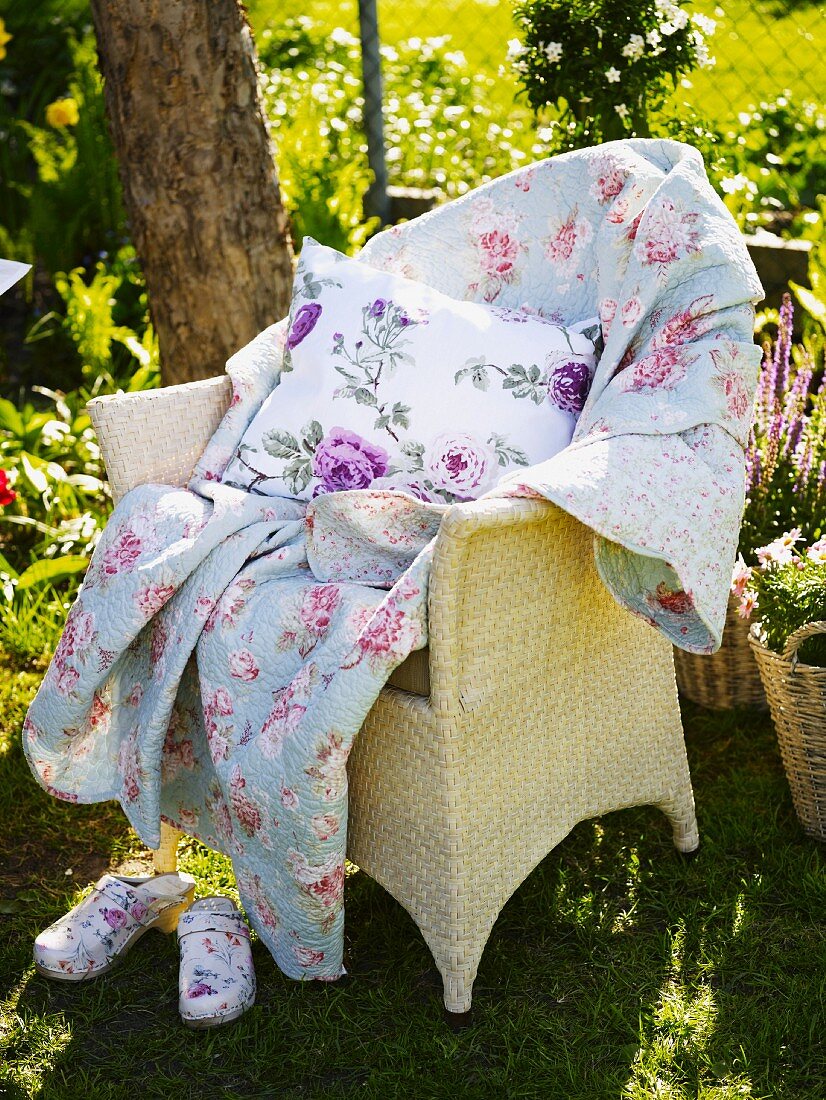 Korbstuhl mit Decke und Kissen im Garten