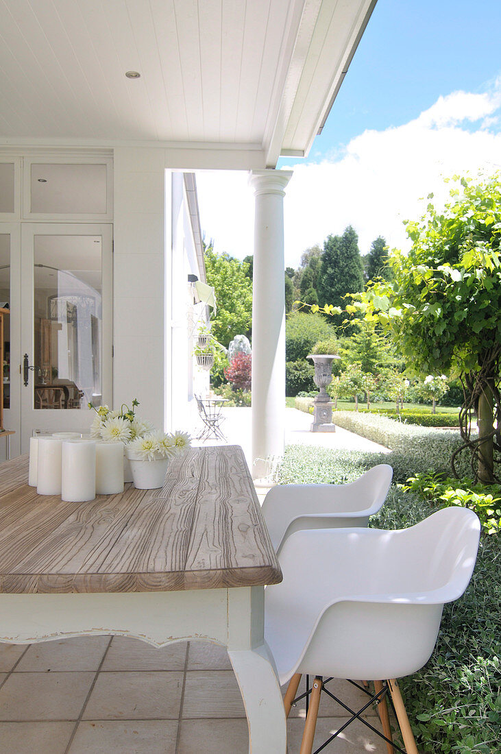 weiße Schalenstühle am rustikalen Holztisch auf Veranda vor Haus im Kolonialstil