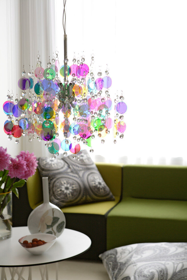 Pendant lamp made of colourful discs above side table in front of green sofa