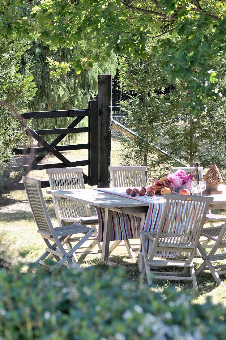 Tisch und Stühle aus Holz im Garten vor geschlossenem Gatter