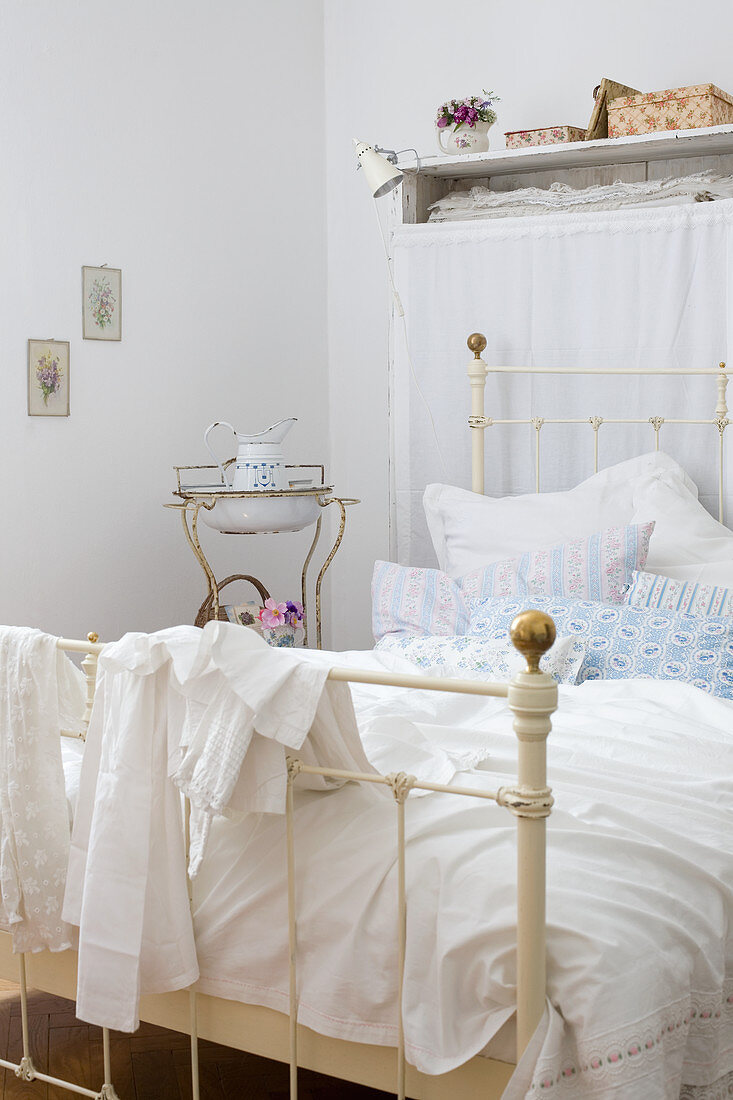Flohmarktflair im Schlafzimmer - Vintage Metallbett mit romantischer Bettwäsche und antikes Waschgestell im Hintergrund