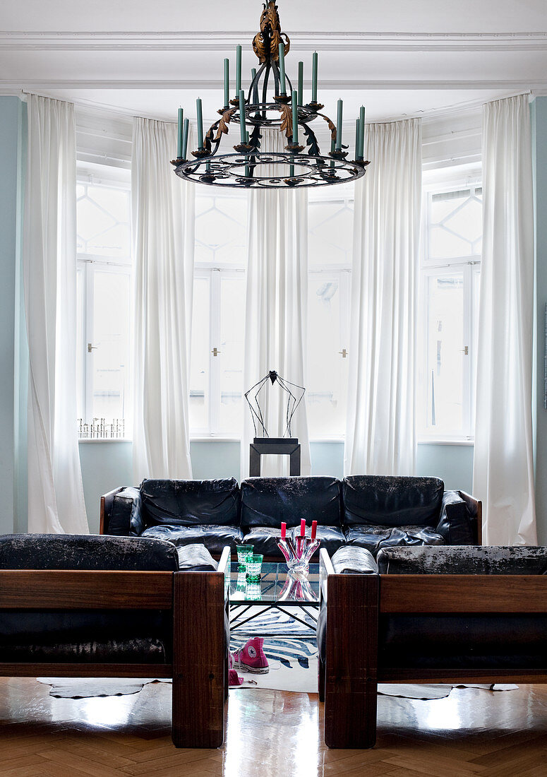 Black 60s designer sofas and wrought iron chandelier in front of bay window in period living room