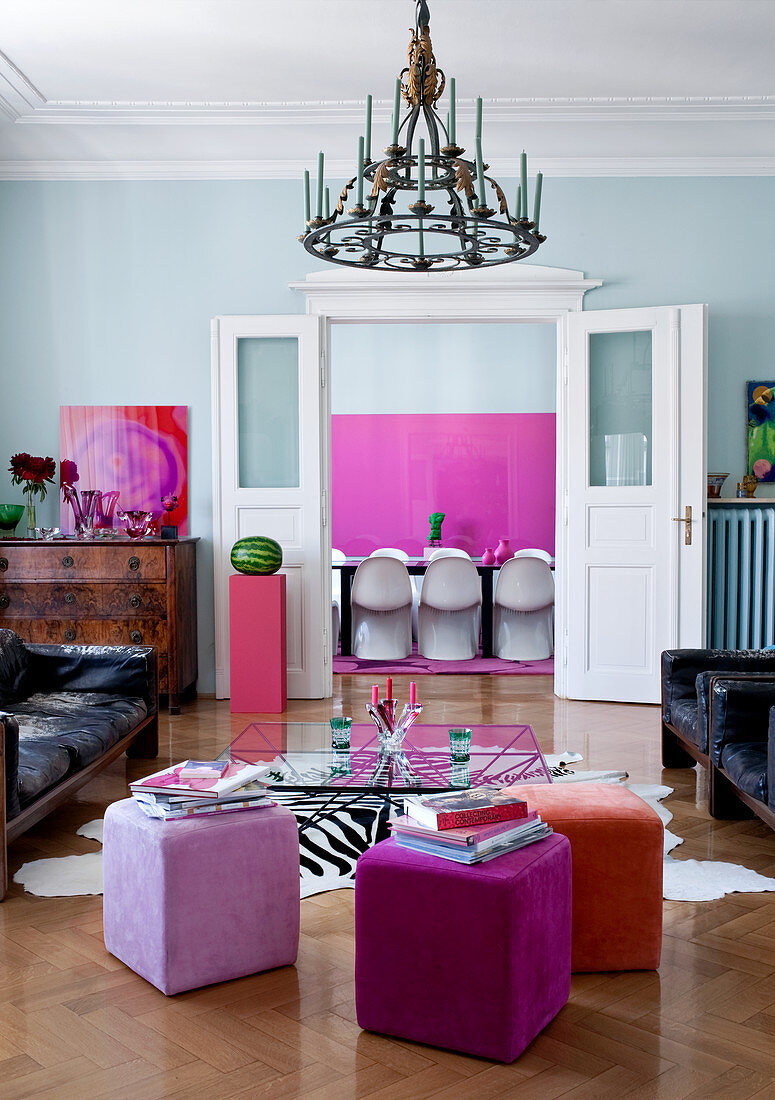 Gelungene Mischung aus Design Klassikern und Antiquitäten im Altbauwohnzimmer, dazu weiße Panton-Chairs vor pinkfarbenem Kunstwerk im Esszimmer