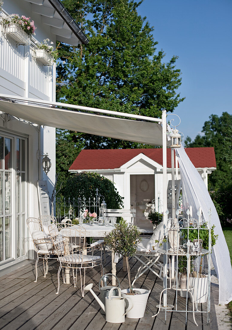 Delicate, white metal chairs on wooden terrace of country house