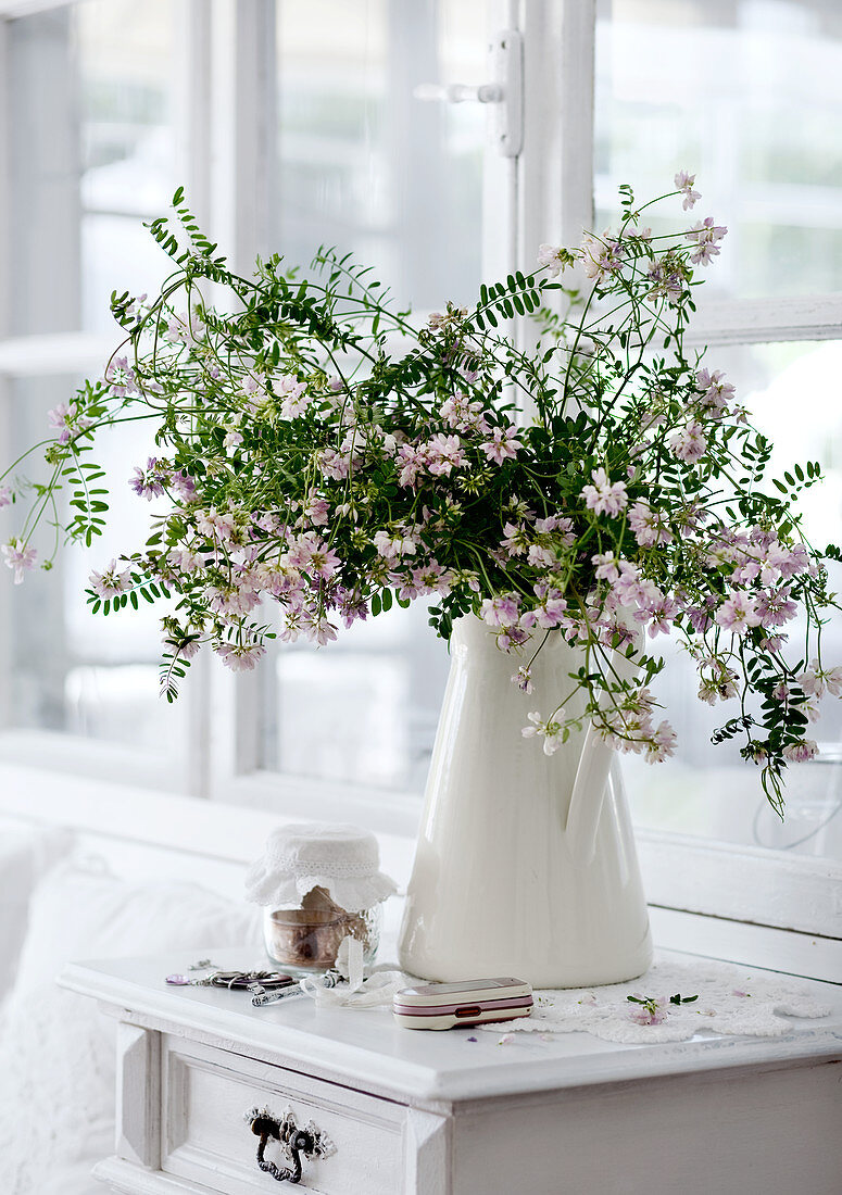 Gartenblumenstrauss in weißem Porzellankrug auf halbhohem Schränkchen