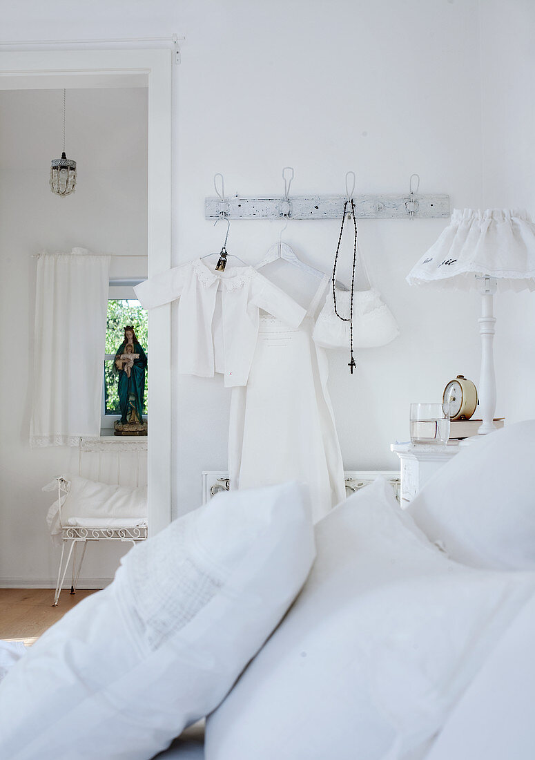 White pillows on bed and child's clothing hanging on wall hooks