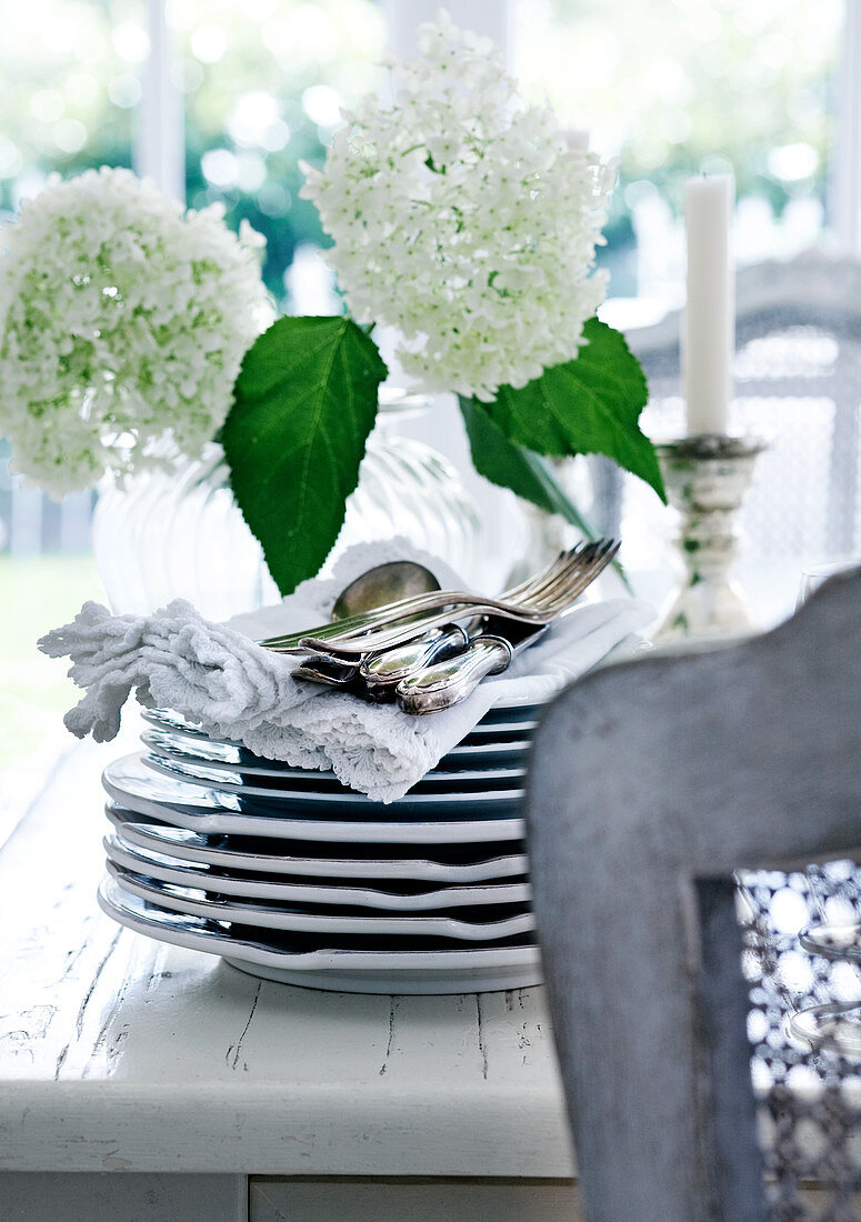 Silver cutlery on stack of plates in front of vase of white flowers