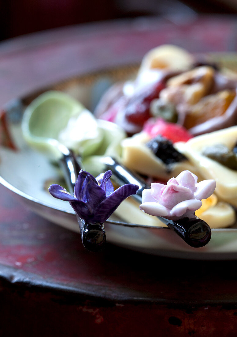Close-up of elegant salad servers with stylised flowers on handles, blurred food on rustic plate in background