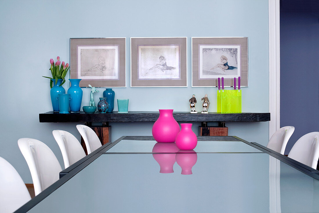 Langer Esstisch mit Pink-Vasen auf Milchglasplatte und weiße Panton Chairs; Bilder und Vasen auf Board im Hintergrund