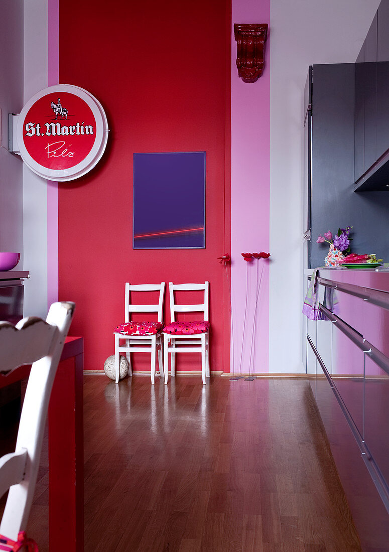 Moderne Wohnküche mit Kunstobjekten und Bierreklame vor knalliger Wandgestaltung in Rosa und Rot