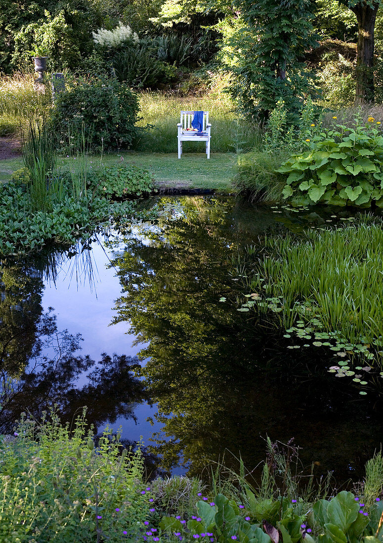 Stuhl steht mit Blick auf den Teich im sommerlichen Garten