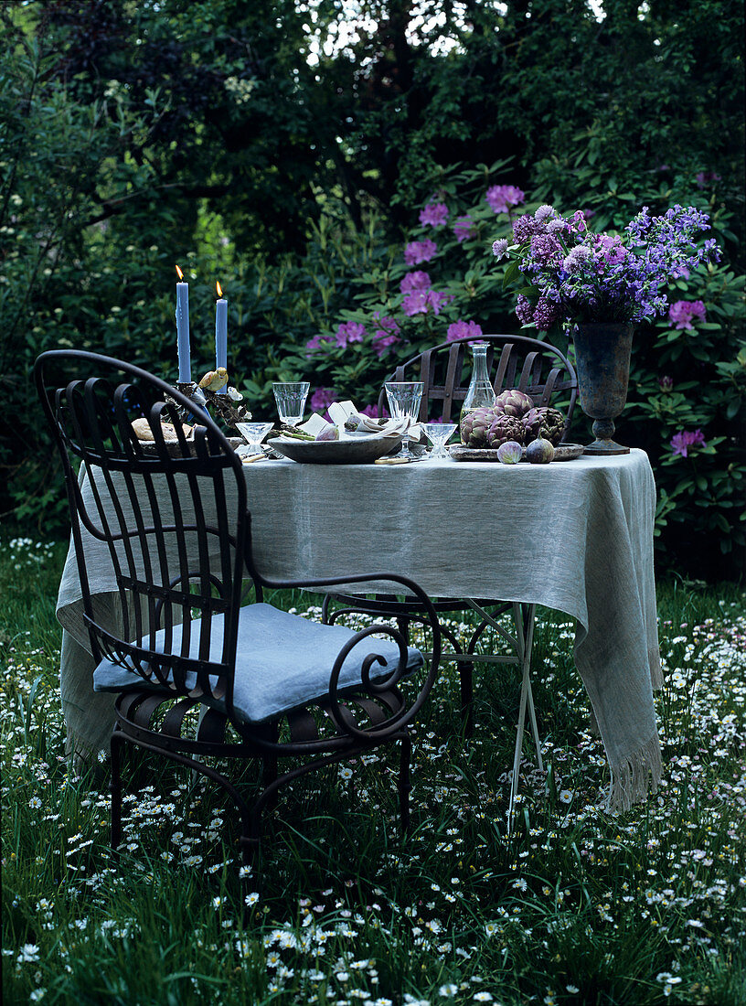 Romantisch gedeckter Tisch mit Kerzenlicht und Blumenstrauss im Garten