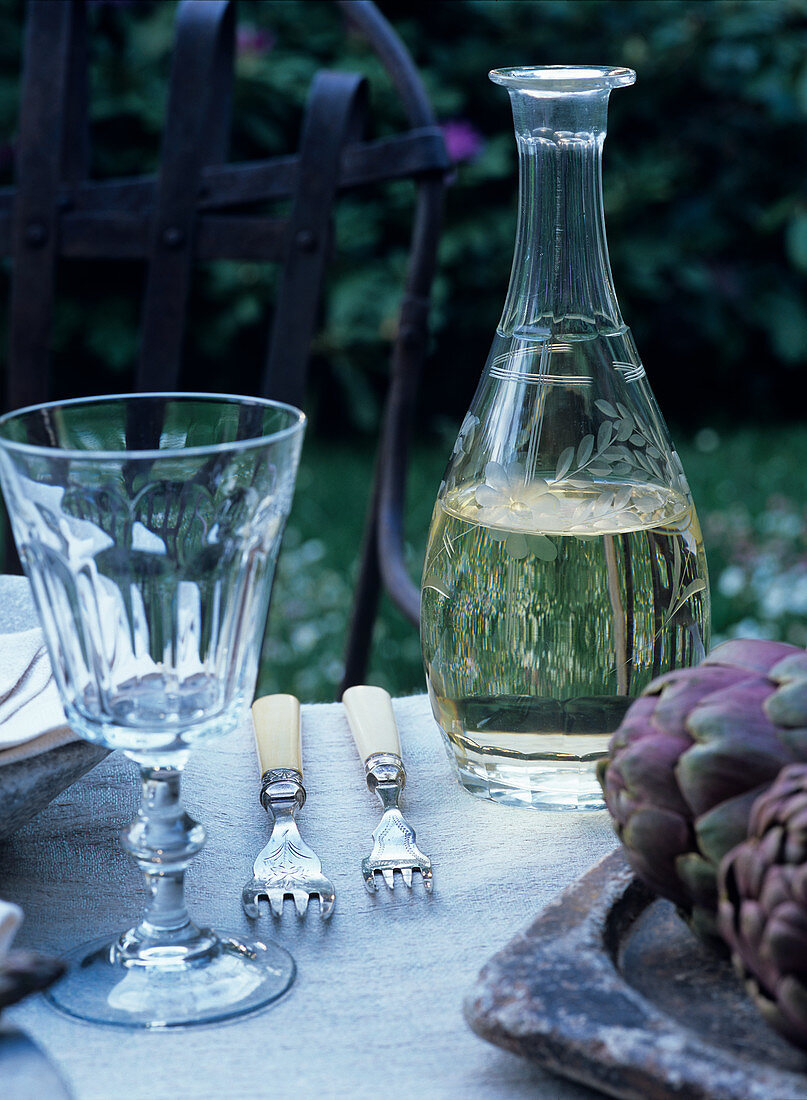 Karraffe mit Weißwein und rustikales Weinglas auf gedecktem Tisch im Garten