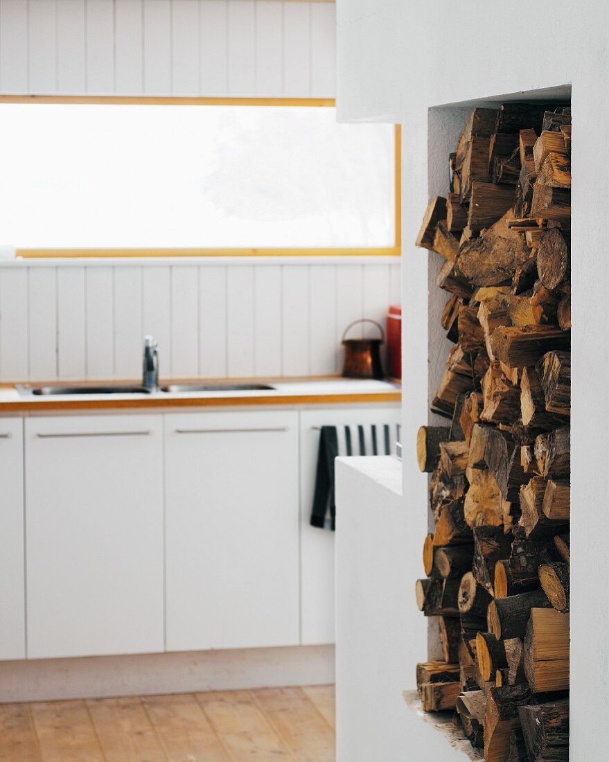 Firewood storage in a wall niche next to a modern kitchen