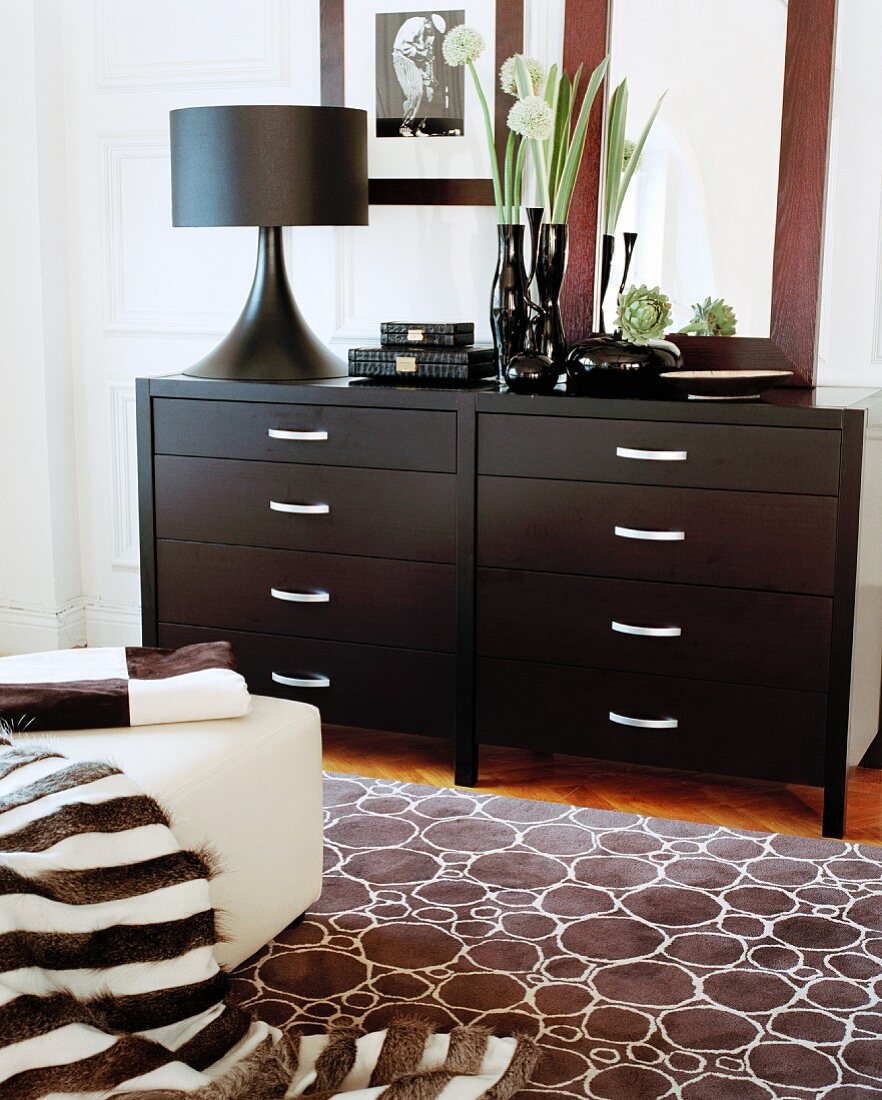 Carpet with circular pattern in front of a chest of drawers made of dark wood and a black table lamp