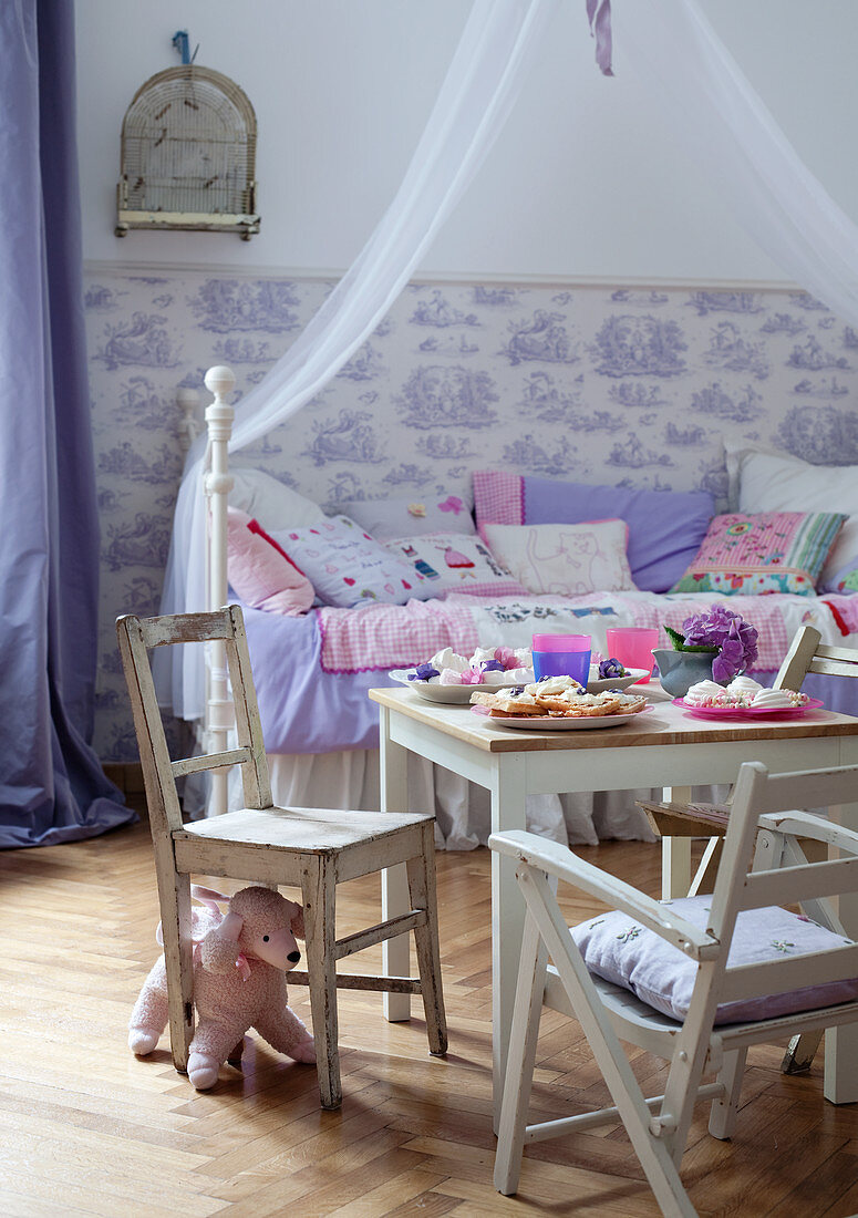 Ländliche Kinderstühle und Tisch mit Süssigkeiten vor Himmelbett im Kinderzimmer