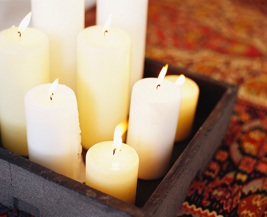 Verschieden grosse Kerzen mit Kerzenlicht auf Holztablett