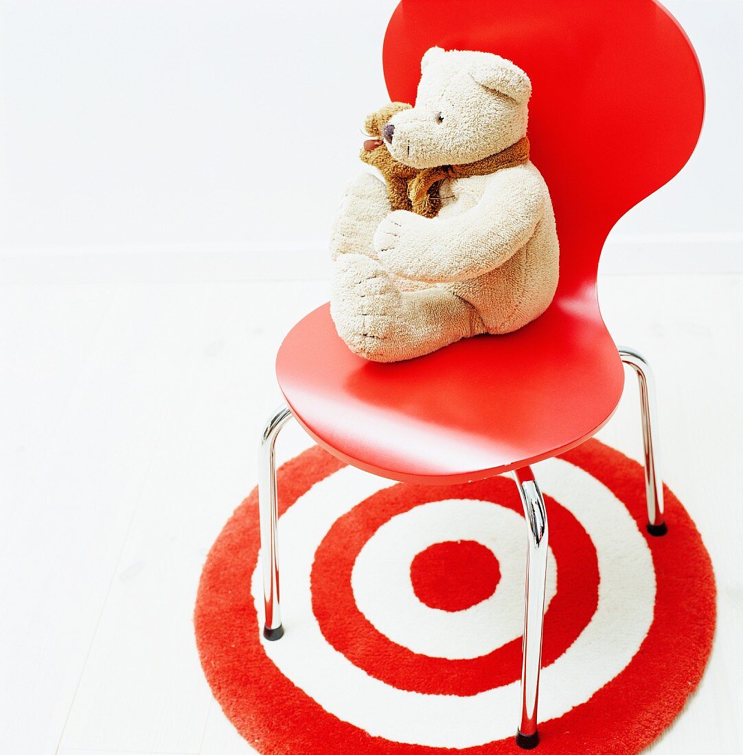 Teddybär auf rotem Schalenstuhl aus Bauhauszeit