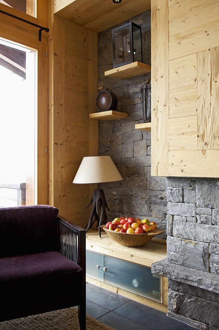 Corner of rustic, modern room with grey stone wall and purple armchair