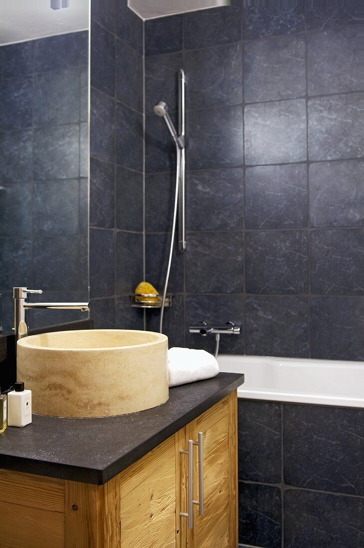 Modern bathroom with stone basin on washstand and dark grey wall tiles