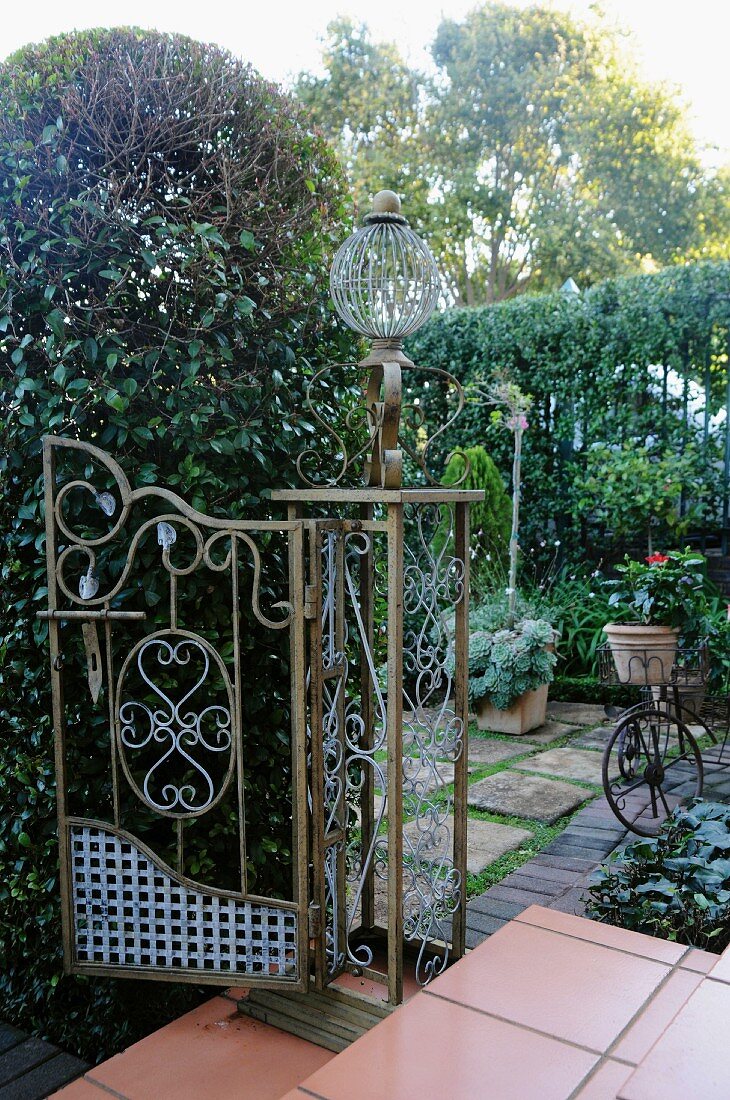 Altes, verziertes Eisentor auf breiten Stufen und Blick in geschützten, romantischen Terrassengarten