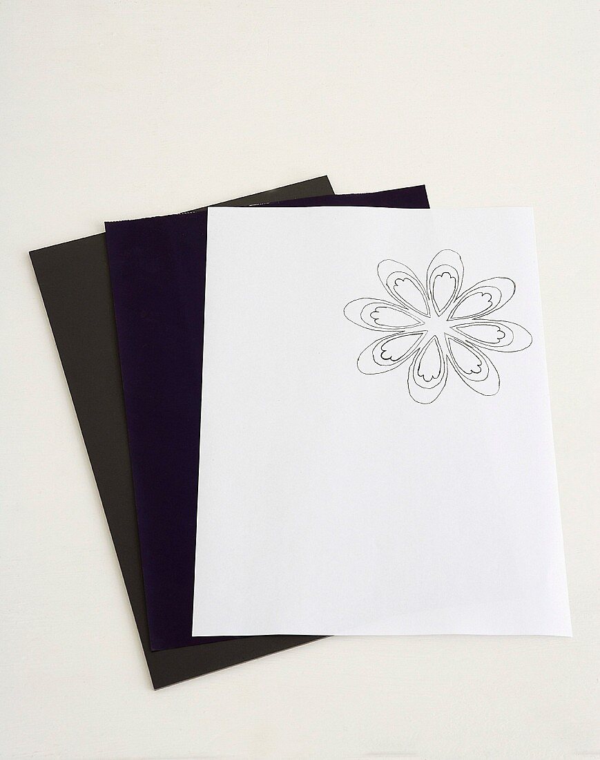 Zeichnung mit Blumenmotiv auf weißem Papier und dunkle Papierbögen