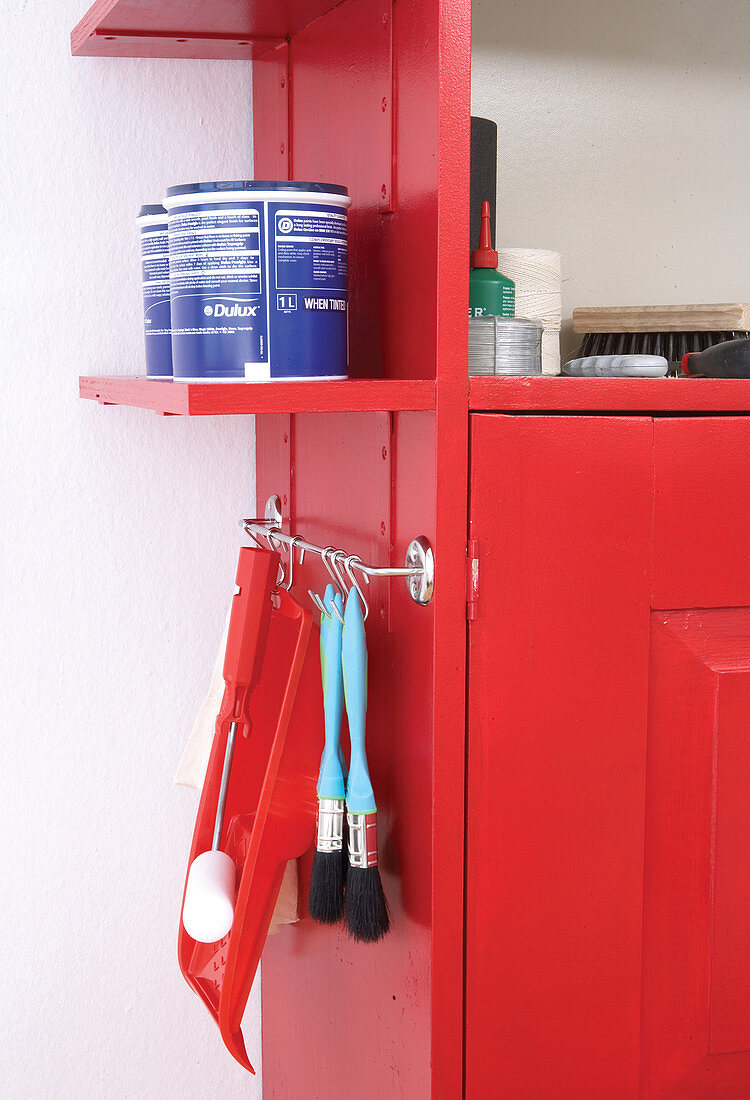 Shelves and hook rail attached to outer wall of red tool cabinet provide extra storage space for paintbrushes and tins of paint