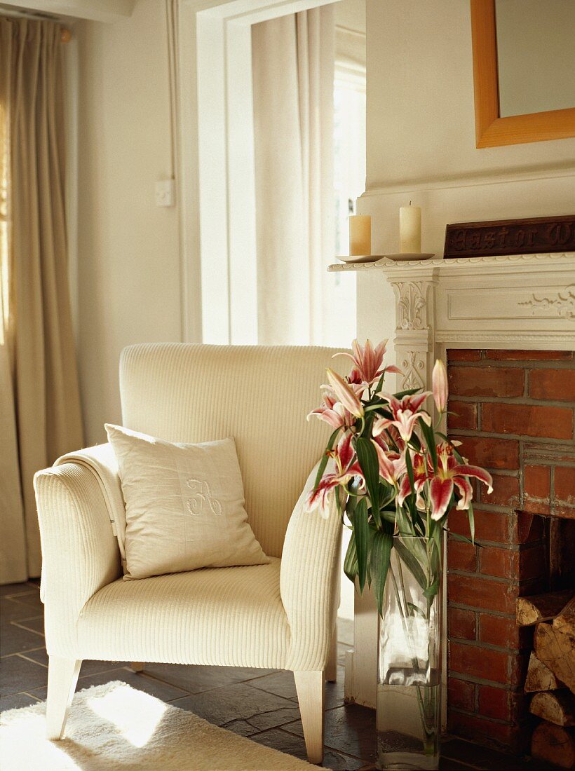 Eleganter Sessel mit weißem Bezug und Lilienstrauss neben gemauertem Kamin