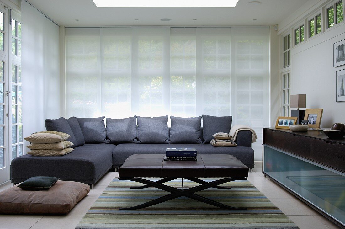 Graues Sofa übereck mit passenden Kissen und Couchtisch mit lederbezogener Tischplatte