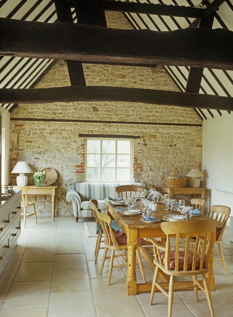 Rustic dining area in open-plan room with stone walls and roof timbers