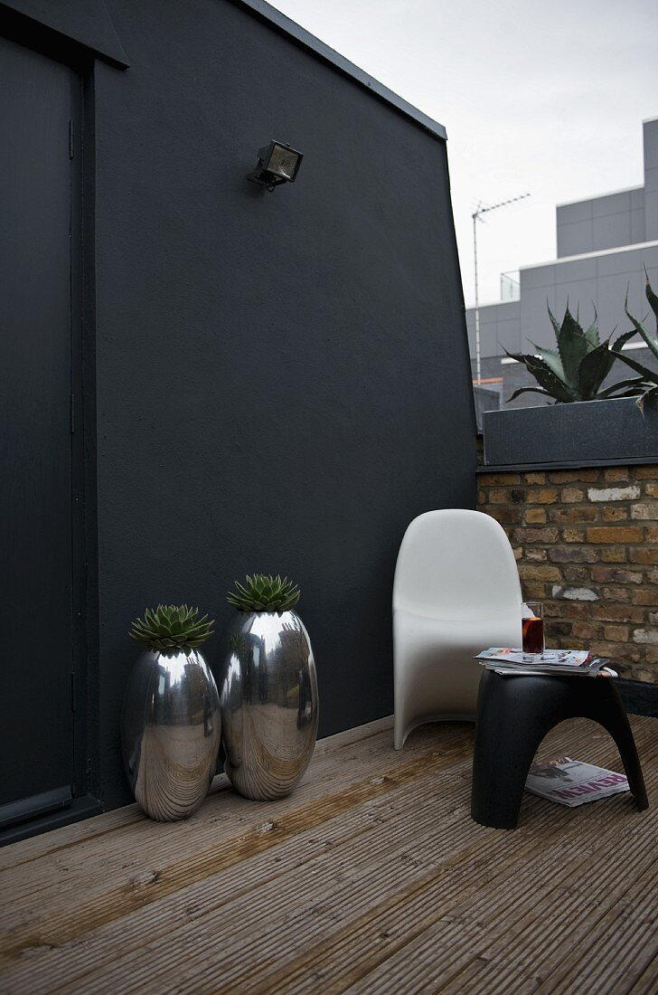 Chrome planters and designer garden furniture against black wall on terrace