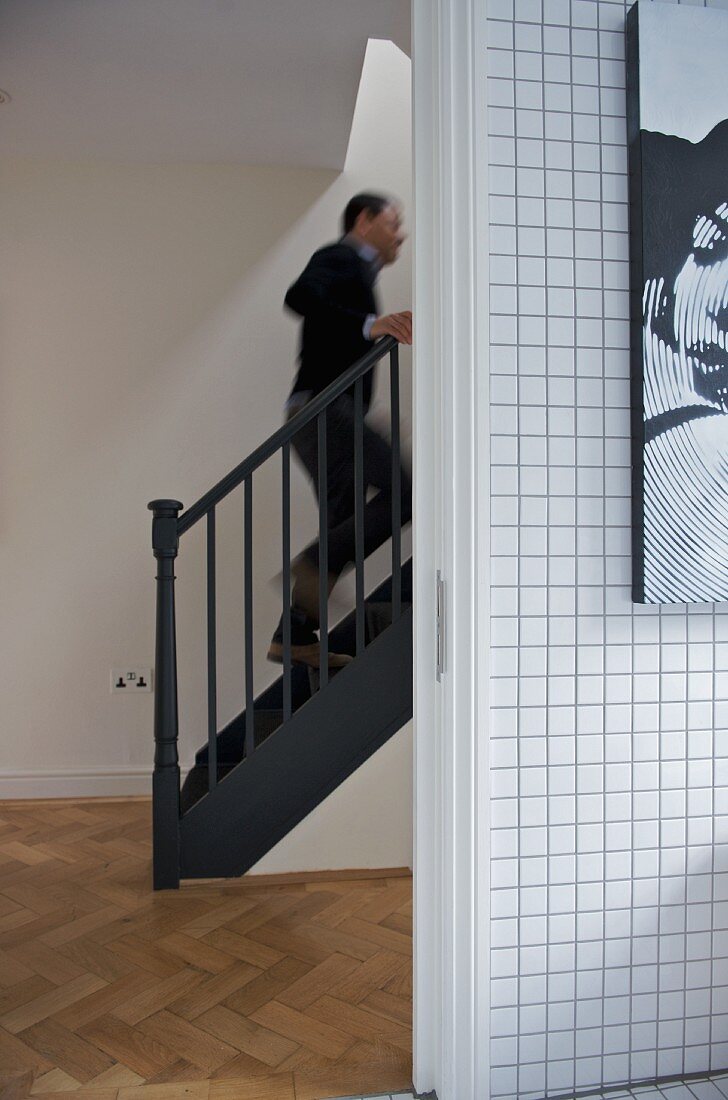 Weiß geflieste Wand neben offenem Durchgang und Blick auf einen Mann im Treppenhaus