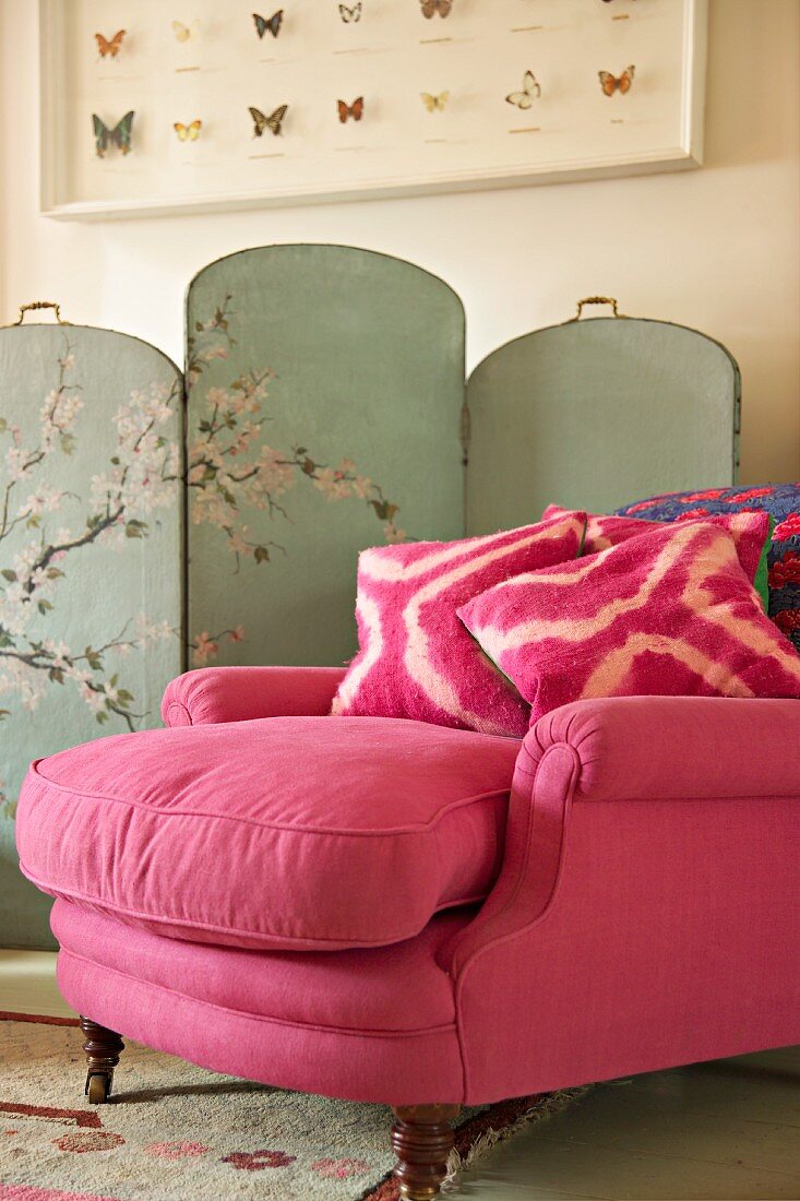 Antique armchair upholstered in pink velvet with cushions in front of painted screen with Chinese motif